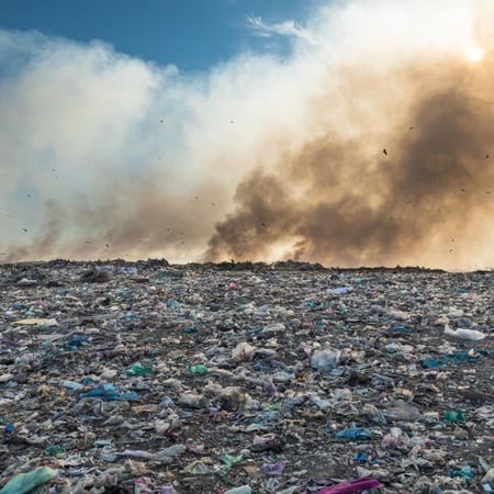 Smoke rising over a wide landfill covered in scattered plastic waste