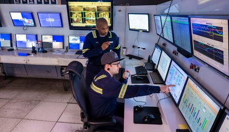 Two plant operators monitoring screens in a facility control room