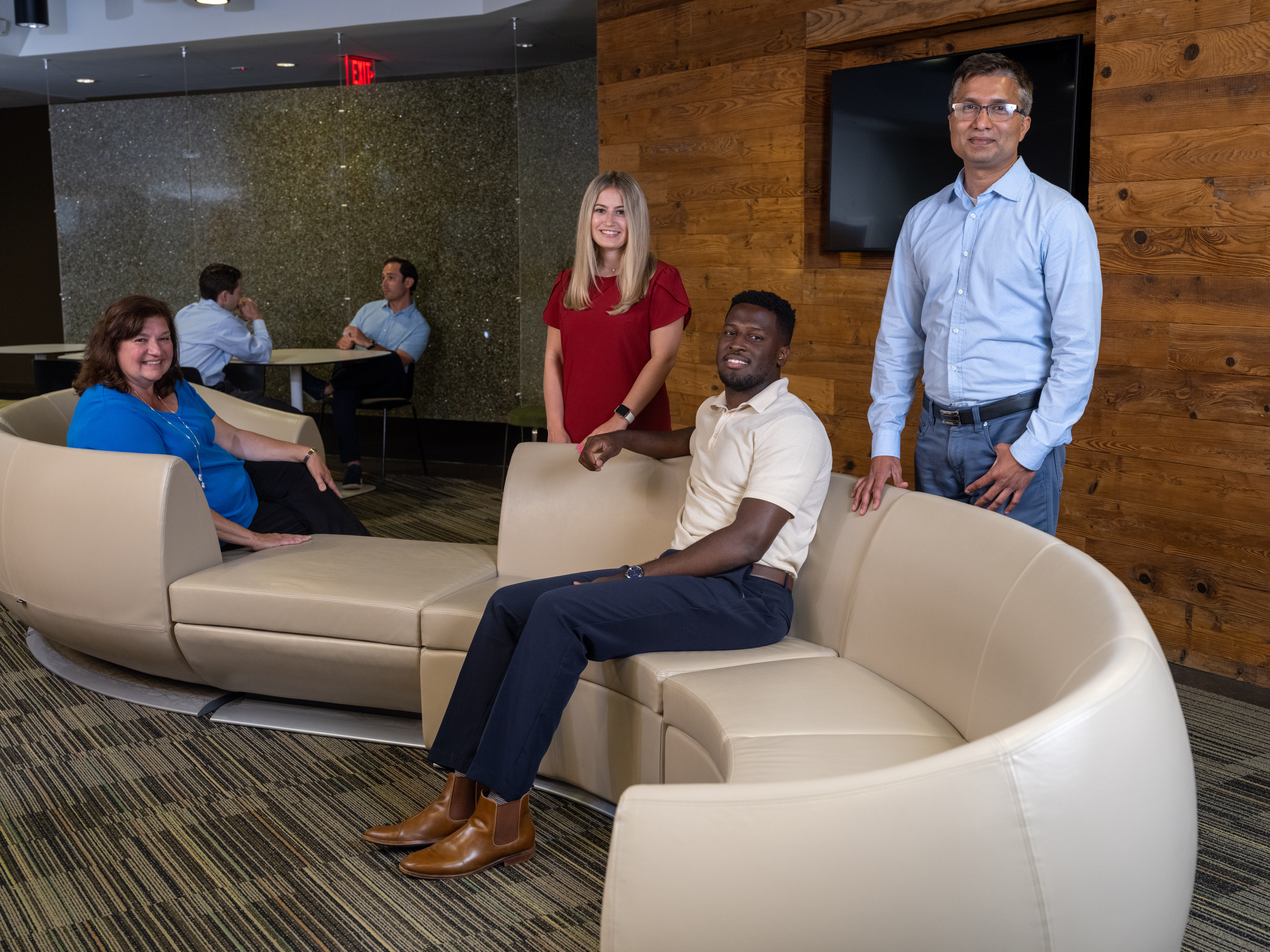  Coworkers talking together in a lounge area with curved seating and a green plant wall