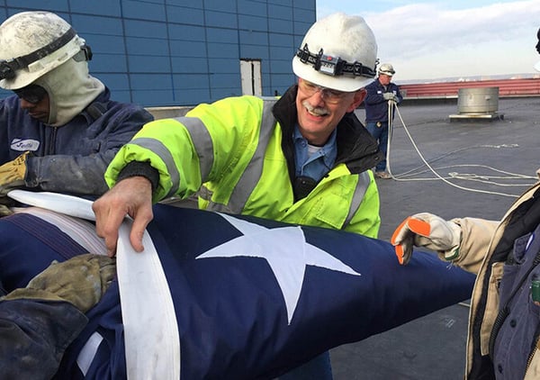 Two Reworld workers in hard hats and high-visibility gear folding an American flag on a facility roof