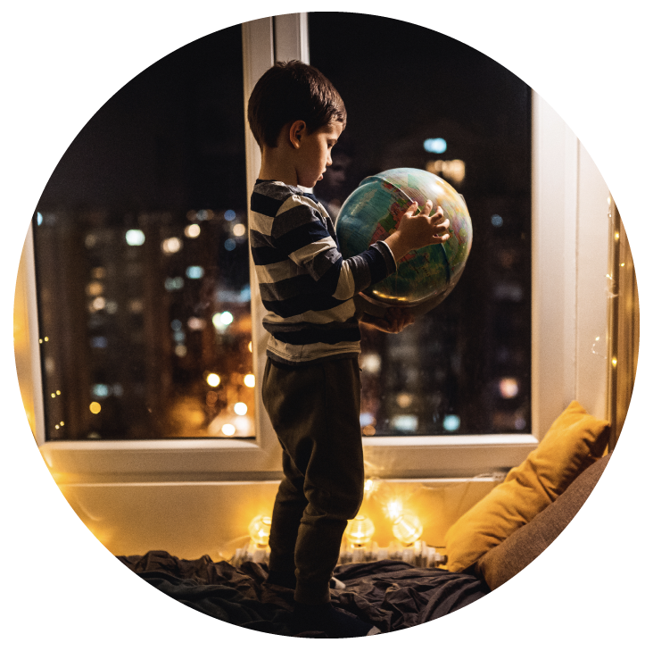 Child standing at a window at night holding a globe, city lights glowing behind
