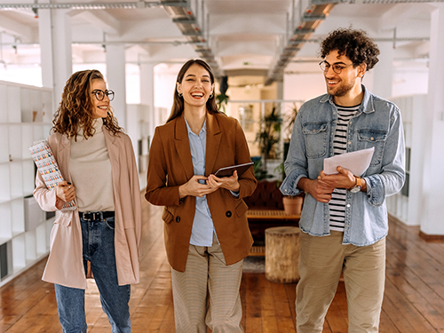 Three early career professionals walking and talking together in a bright open office