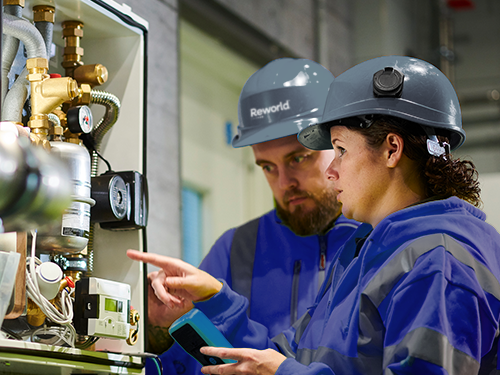 Reworld employees in hard hats inspecting equipment gauges and controls at a facility