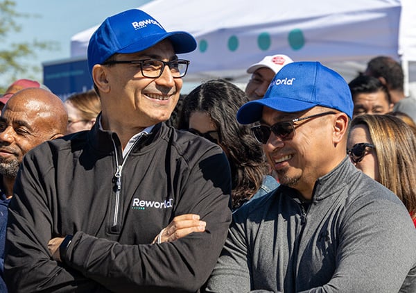 Reworld employees in branded caps and jackets smiling together outdoors at a company event