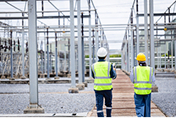 Two men walk in an electric utility switchyard.