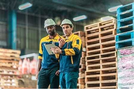 Two workers in a warehouse reviewing materials and coordinating a waste management program.