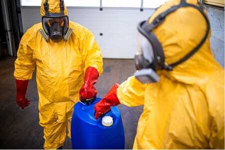 Workers in protective gear handling regulated waste containers at an industrial facility.