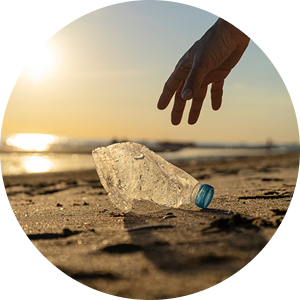 Gloved hand picking up a discarded plastic bottle from a beach at sunset