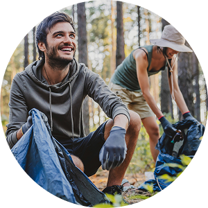 Two volunteers collecting litter into blue bags in a wooded area