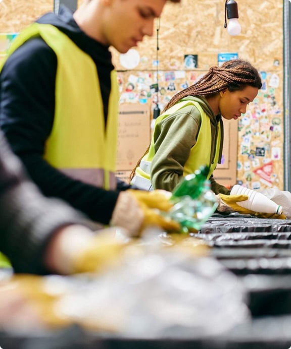 Two workers in high-visibility vests sorting recyclable materials on a conveyor line