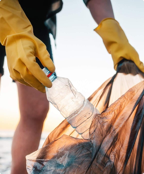 Gloved hands gathering collected litter into a bag during a beach cleanup