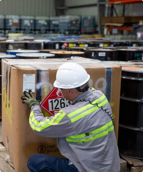 Worker at Reworld facility checks tag on hazardous waste shipment.