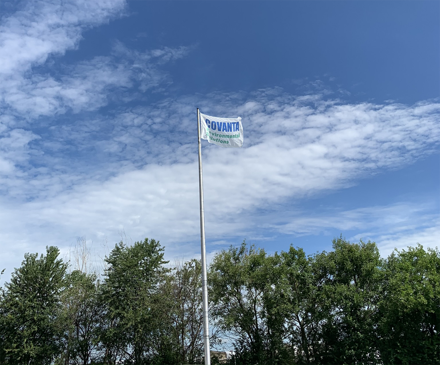 Covanta Environmental Solutions flag waving on blue sky above the tree line